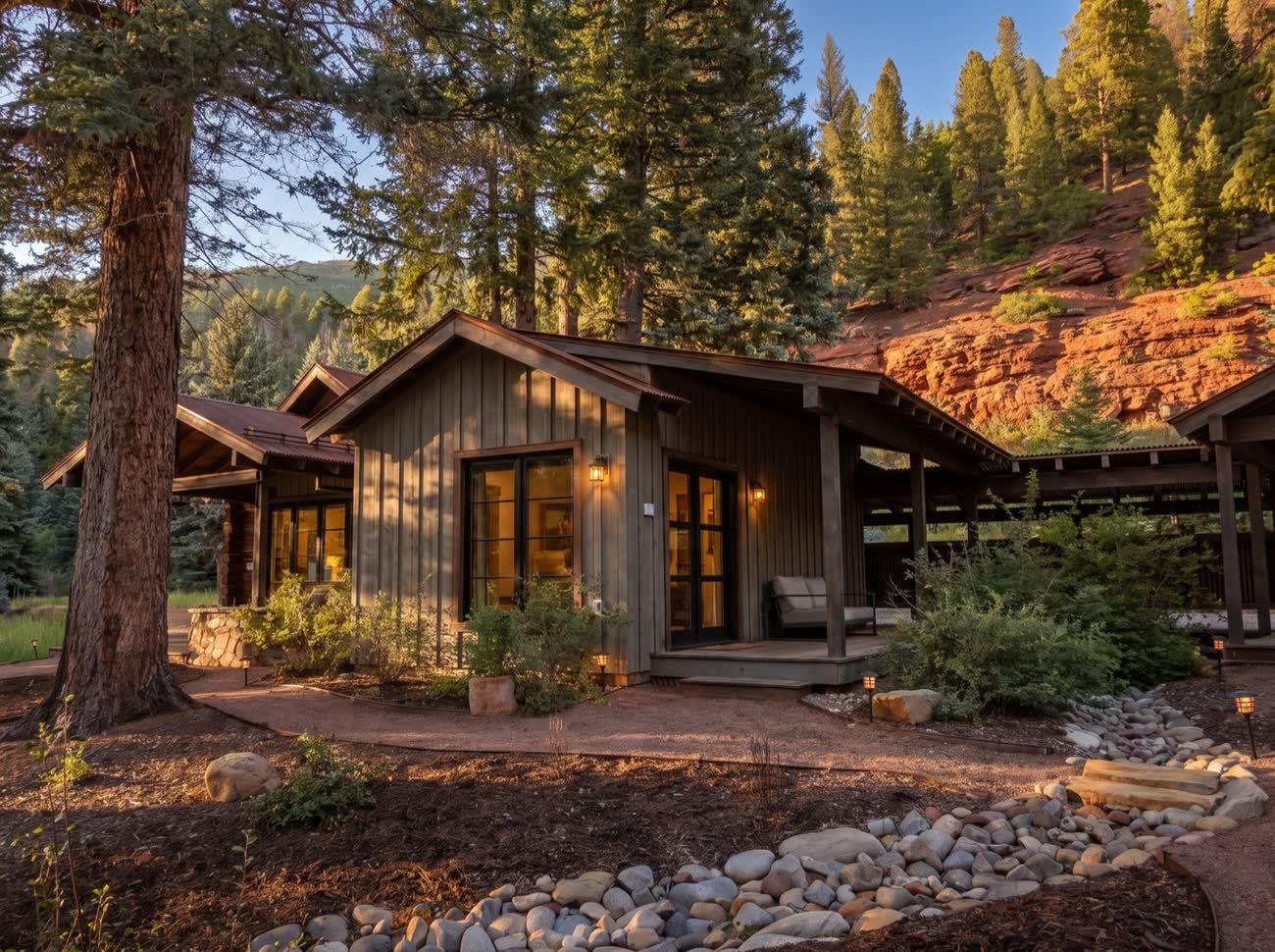 Cabins lit at dusk among ponderosa pines below red rock