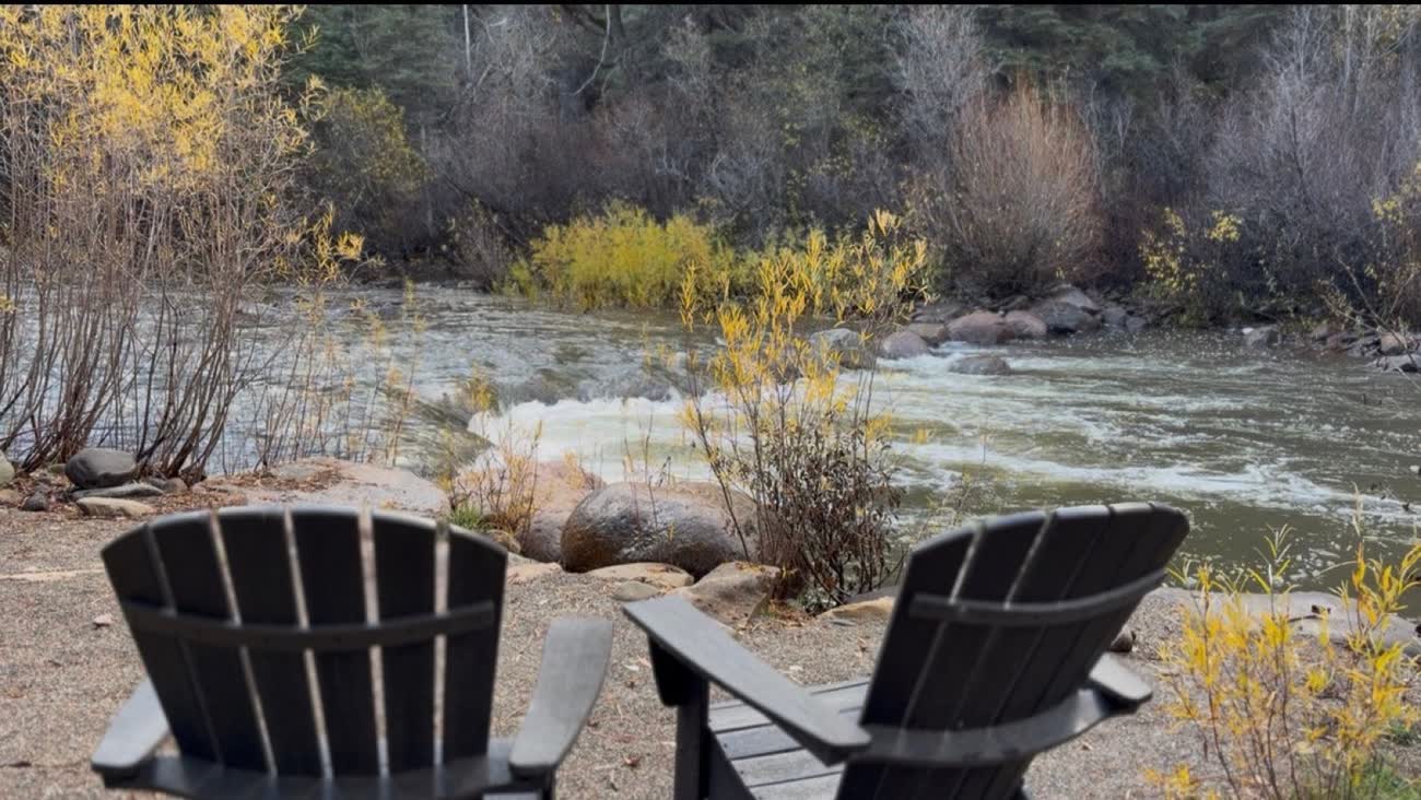 Two Adirondack chairs on the bank of the Dolores River with autumn willows